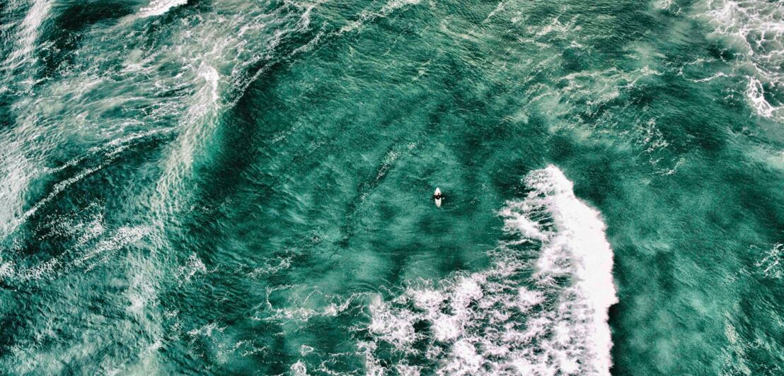 Wellenreiter:in auf einem Brett umgeben von Wasser