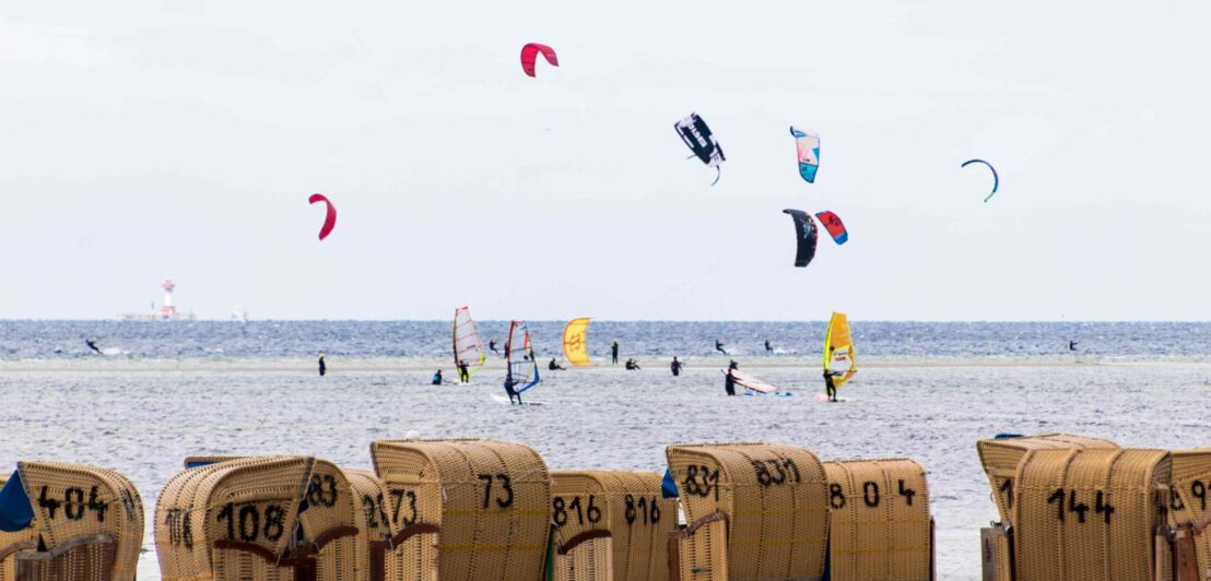 Strandkörbe an Land und Surfer:innen im Wasser in der Ostsee