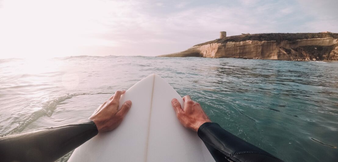 Mann auf einem Surfbrett steuert auf eine Küste zu