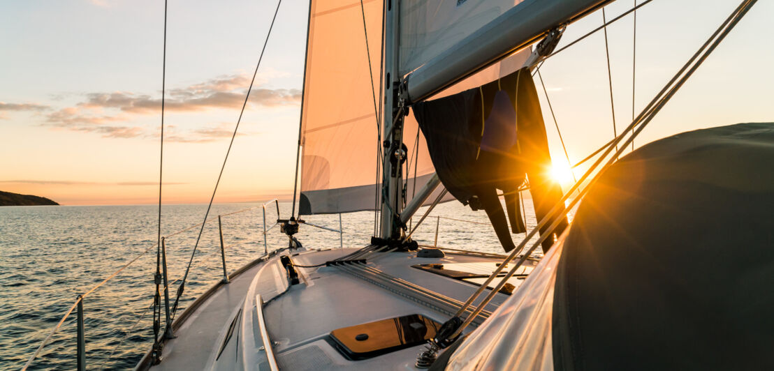 Ein Segelboot steuert auf den Sonnenuntergang zu.