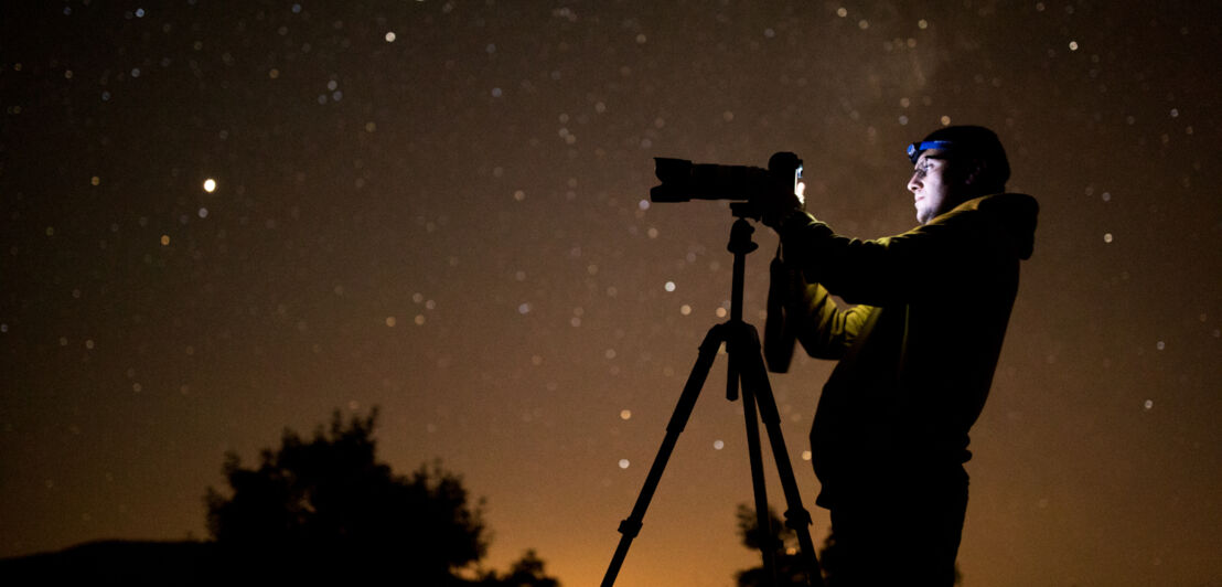 Ein Mann mit Stirnlampe fotografiert nachts