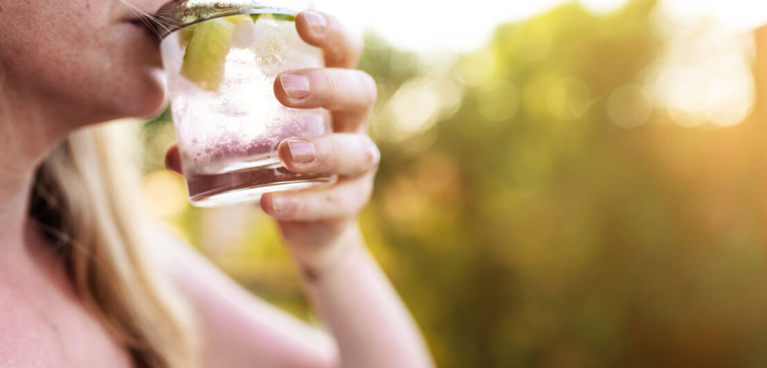 Eine Frau trinkt ein Glas Gin Tonic mit Eis und Zitrone