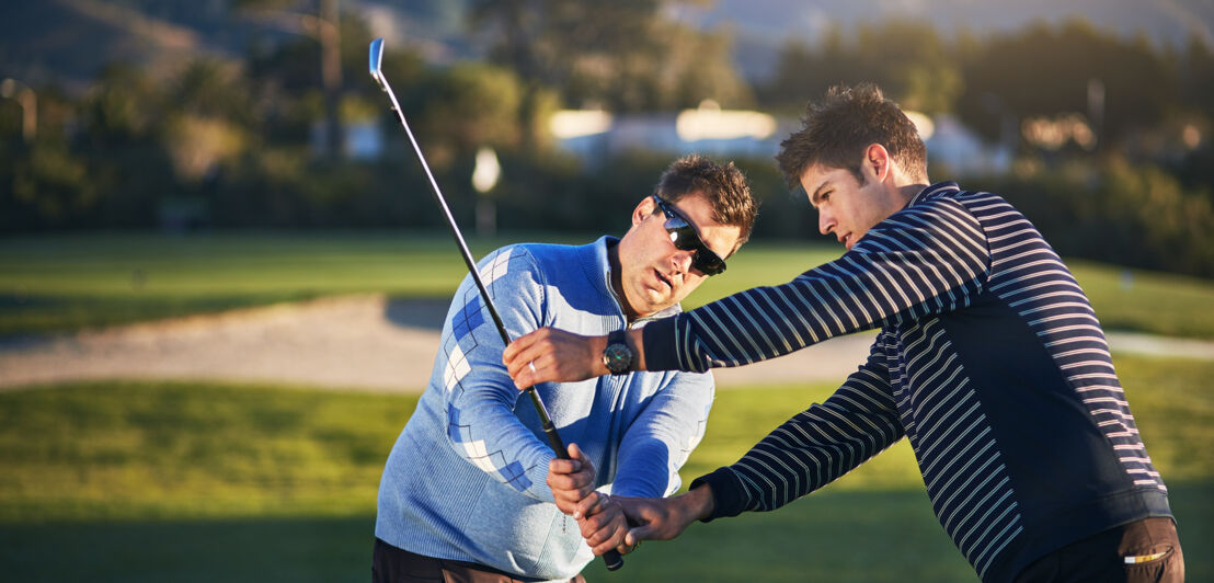 Ein Mann korrigiert die Haltung einer Frau mit einem Golfschläger.