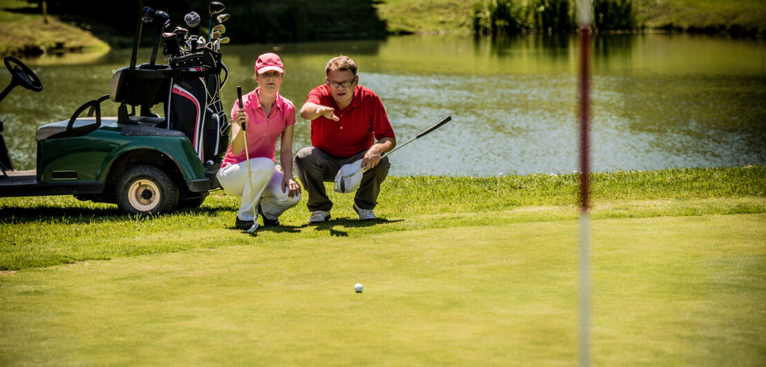 Ein Mann und eine Frau mit Golfequipment in der Hocke, er deutet in die Ferne