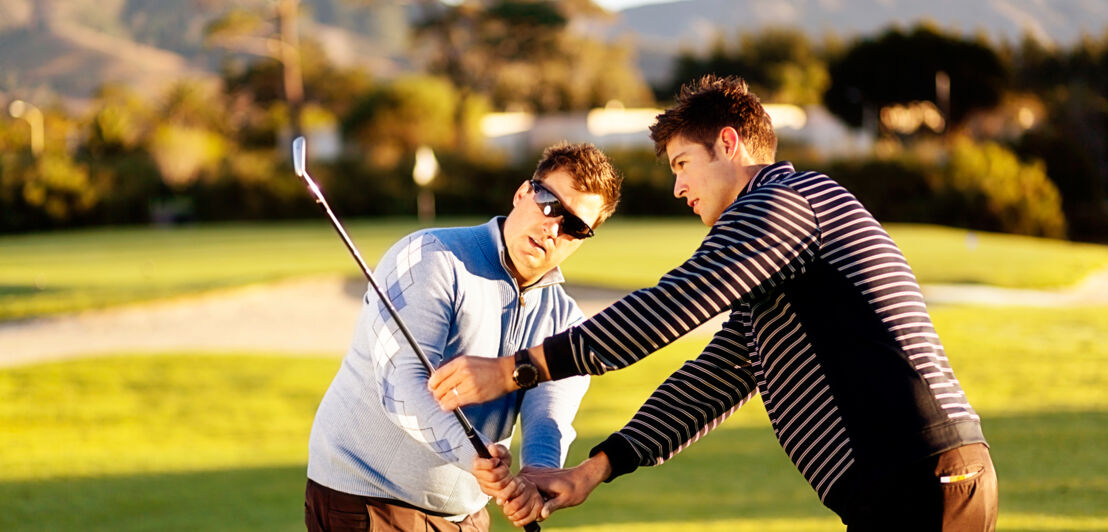 Ein Golflehrer korrigiert die Schlägerhaltung bei seinem Schüler