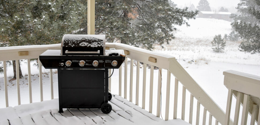 Ein verschneiter Grill steht auf einer Holzveranda