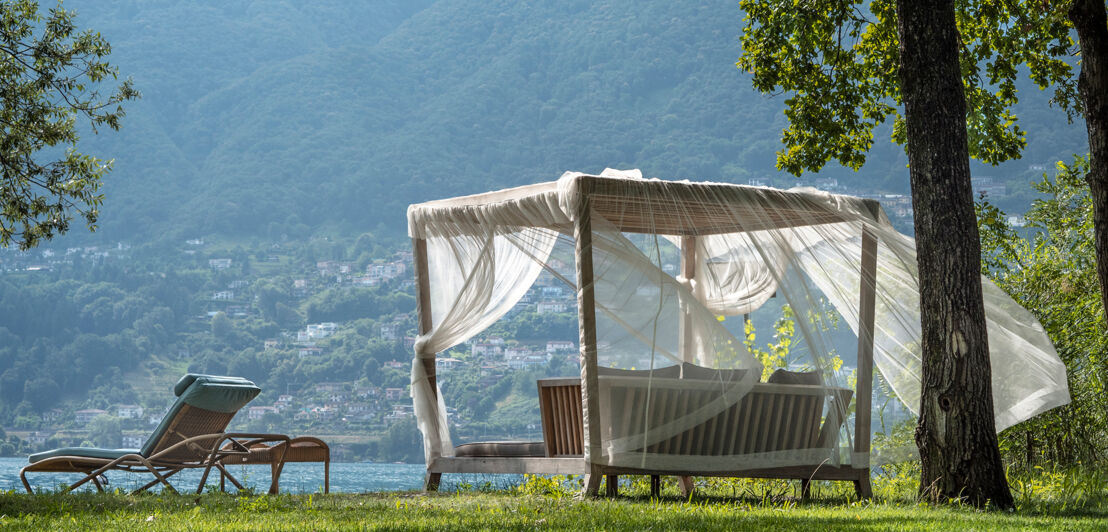 Gartenliege und Sitzgruppe mit Baldachin auf Rasen am Seeufer