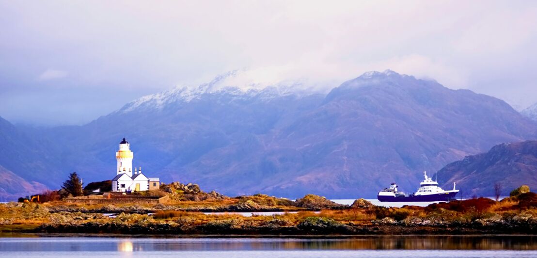 Ein weißer Leuchtturm nahe der Isle of Skye vor Bergpanorama