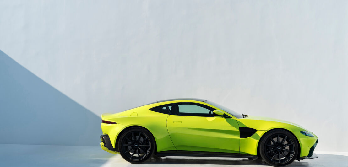 Ein Aston Martin Vantage in gelb-grüner Autofarbe Lime Essence vor einer weißen Wand