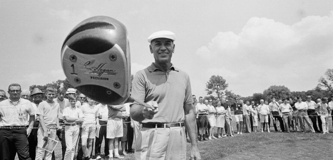 Ben Hogan hält seinen Schläger auf dem Golfplatz in die Kamera, im Hintergrund steht Publikum