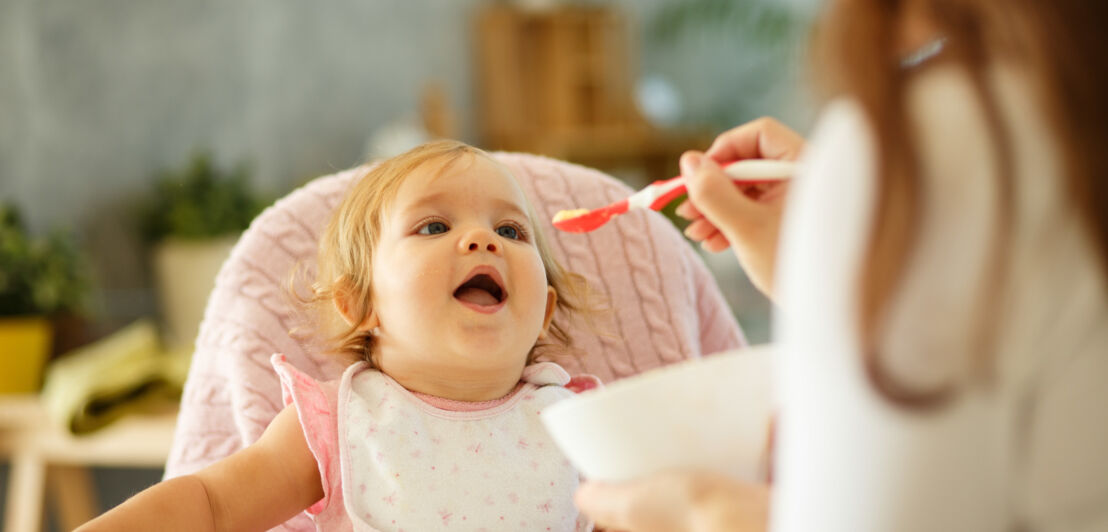 Mutter füttert ihr Baby am Tisch mit Brei