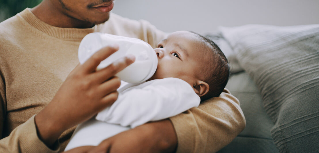 Mann hält Baby im Arm und gibt ihm Fläschchen