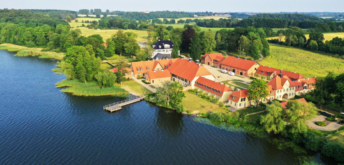 Blick von oben auf ein Gut mit Herrenhaus an einem See