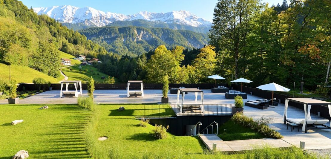 Terrassenbereich mit Wiese und überdachten Liegen, umgeben von Natur mit Blick auf Bergpanorama