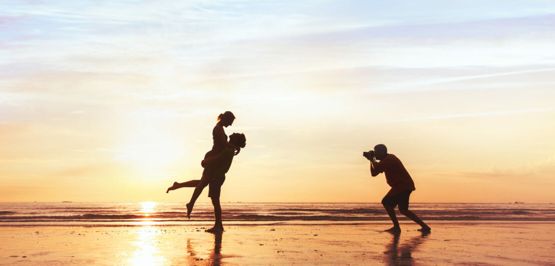 Ein Paar wird am Meer bei Sonnenuntergang fotografiert.