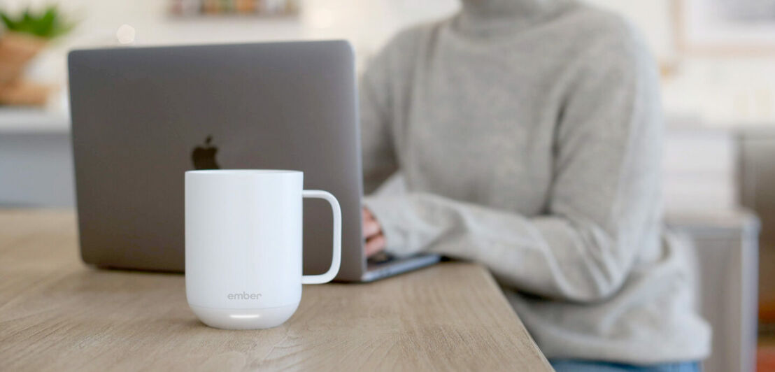 Eine weiße Keramiktasse steht vor einem Laptop