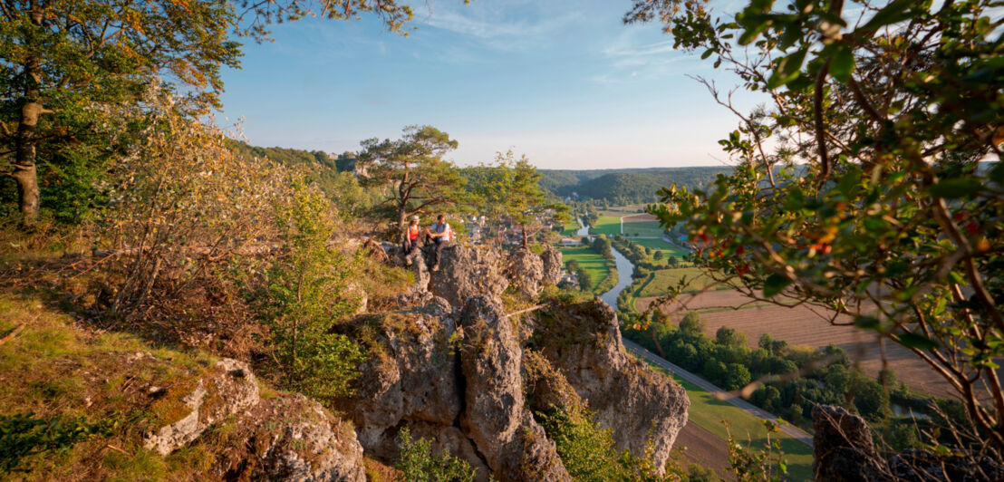 Zwei Wander:innen sitzen auf einem Felsen hoch über der Altmühl