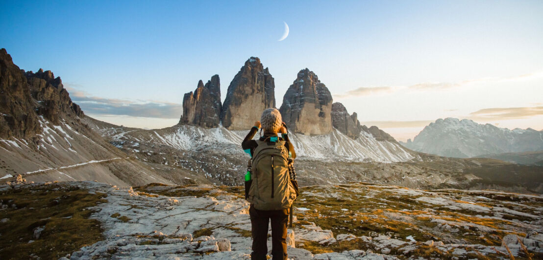 Ein Wanderer fotografiert eine Landschaft mit Mond bei Tageslicht.