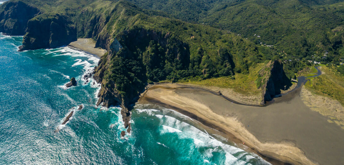 Blick von oben auf türkisfarbenes Wasser, einen einsamen Sandstrand und bewaldete Hügel