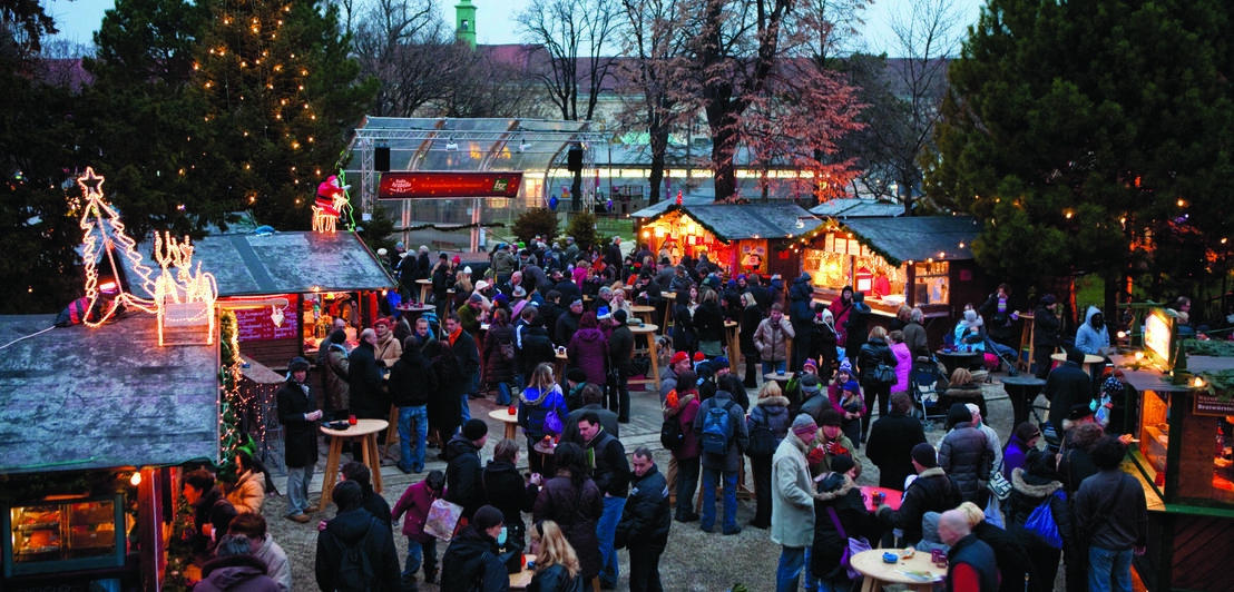 Weihnachtsmarkt mit Menschenansammlung umgeben von Verkaufsständen in der Dämmerung