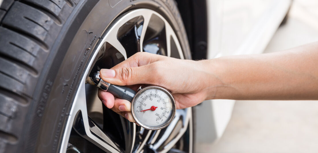 Eine Hand hält einen kleinen, manuellen Reifendruckmesser an das Ventil eines Autoreifens