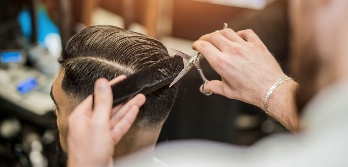 Rückansicht eines Mannes, der von einem Barbier die Haare geschnitten bekommt