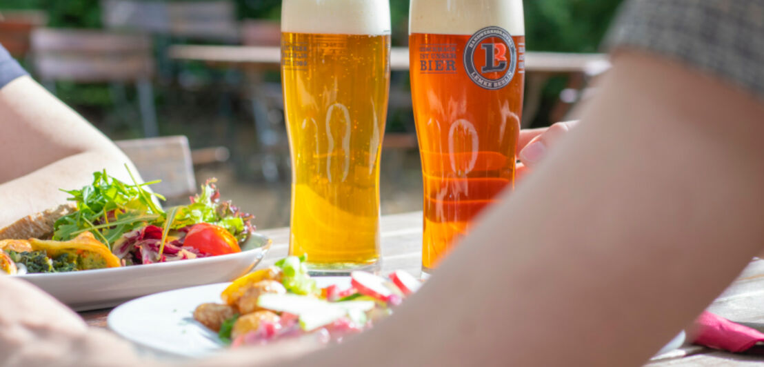 Zwei Gläser mit Bier und zwei gefüllte Teller mit Salat auf einem Tisch