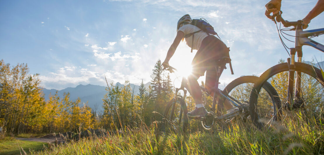 Zwei Radfahrer überqueren eine Wiese vor einem Bergpanorama