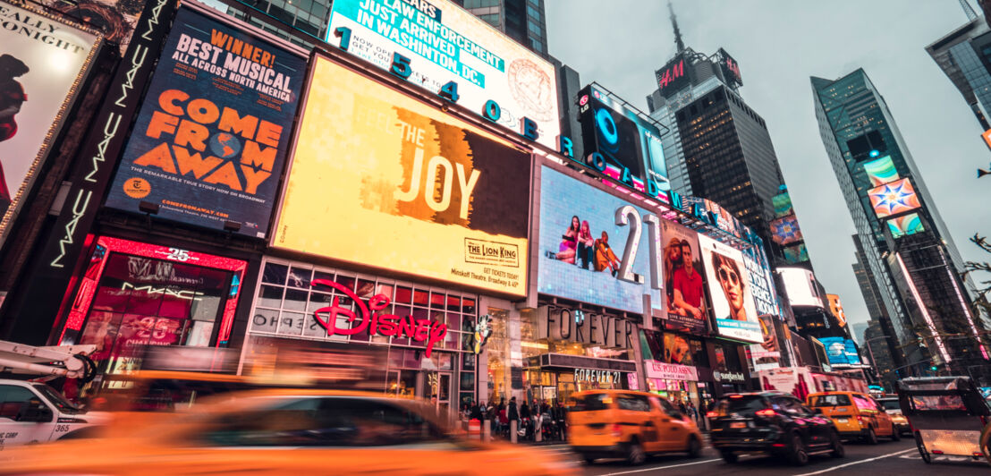 Times Square mit Leuchtreklame und vorbeifahrenden gelben Taxis