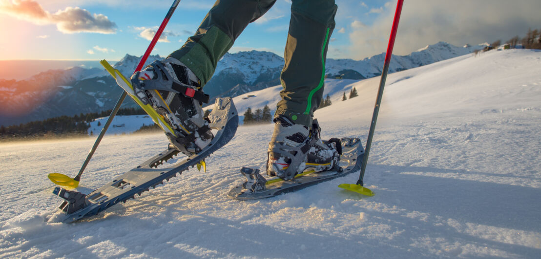 Nahaufnahme der Beine und Füße einer in Schneeschuhen wandernden Person mit Stöcken