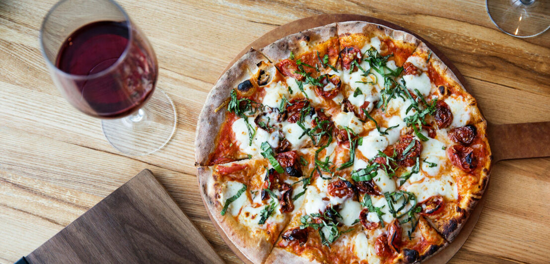 Ein Glas Rotwein und eine Pizza, von oben fotografiert