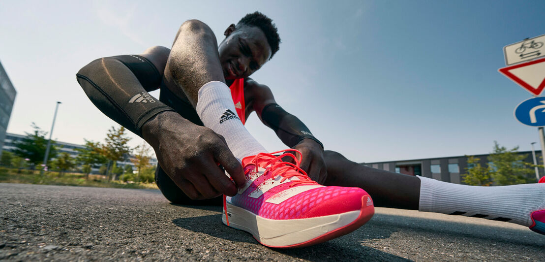 Ein athletischer Läufer sitzt auf dem Asphalt und bindet seinen Sportschuh zu