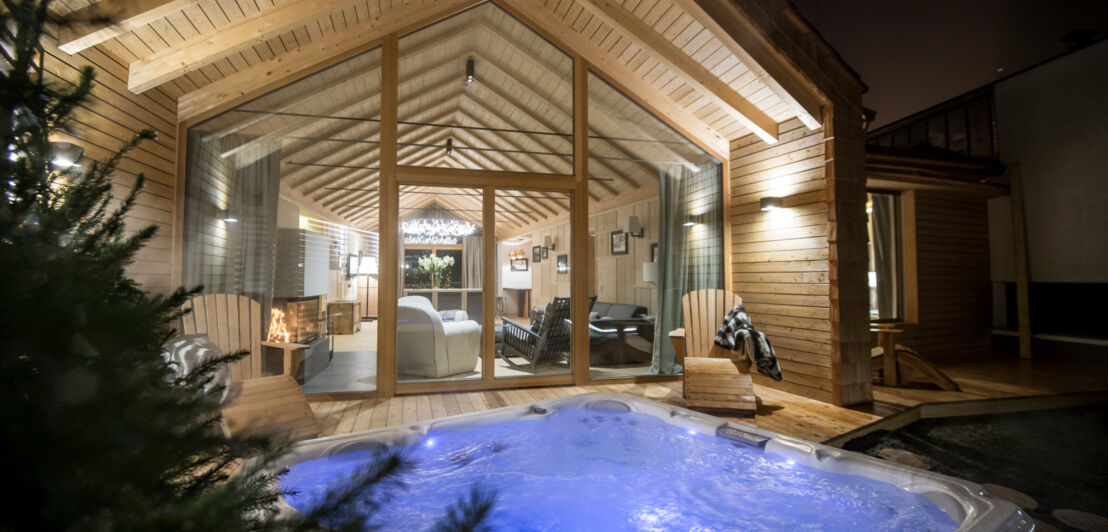 Ein beleuchteter Jacuzzi vor einem Chalet mit großen Holzfenstern