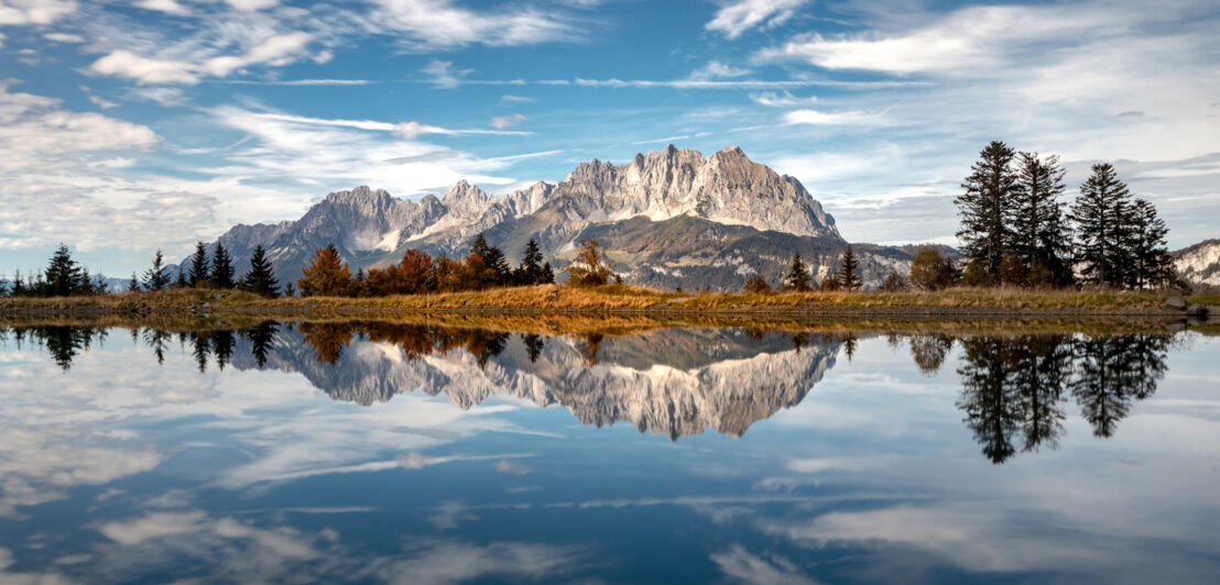 Das Gebirge Wilder Kaiser vor einem Gewässer, darin seine Spiegelung