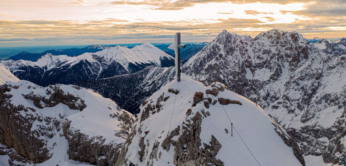 Berggipfel mit Gipfelkreuz vor schneebedeckter Bergkulisse