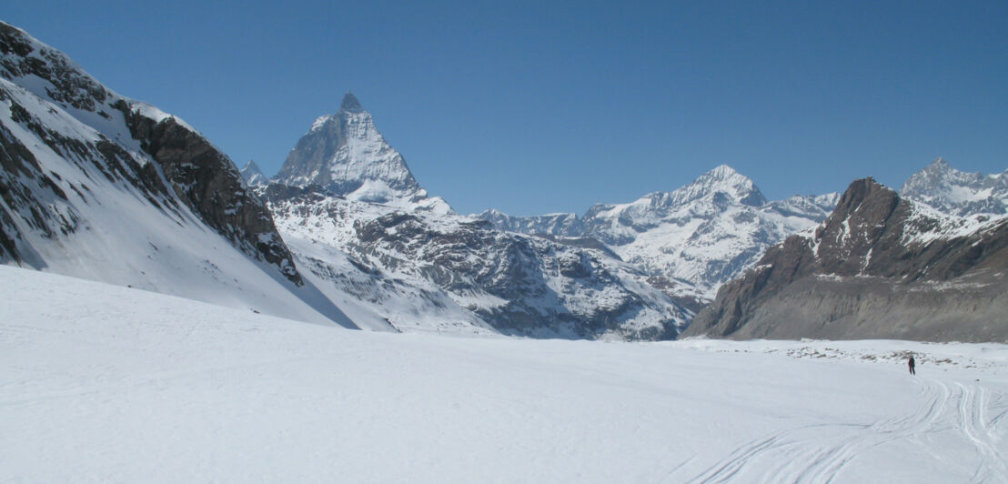 Ein Skifahrer fährt in einer weiten Ebene durch Tiefschnee, im Hintergrund verschneite Gipfel