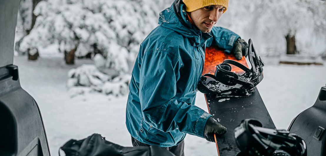 Ein junger Mann packt ein Snowboard ins Auto