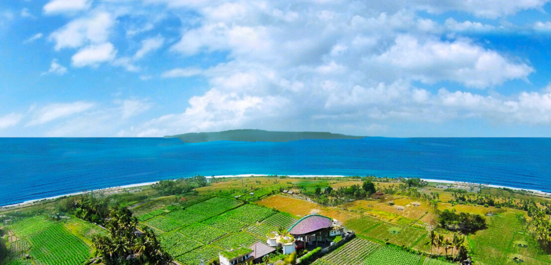 Zwischen grünen Feldern und dem Meer steht eine Hotelanlage auf Bali