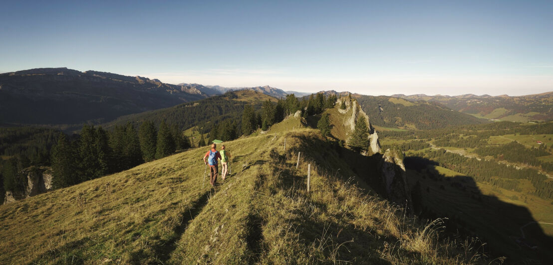 Zwei wandernde Personen auf einem Gipfelgrat, rundherum Berge