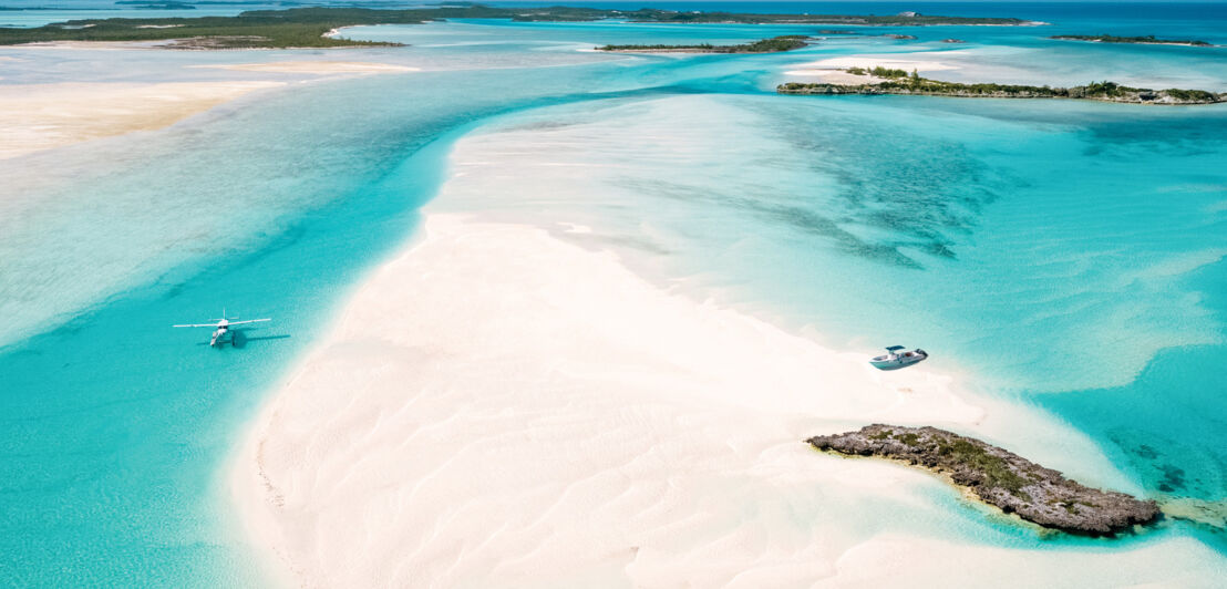 Heller Strand und türkisblaues Meer, auf dem ein Wasserflugzeug landet.