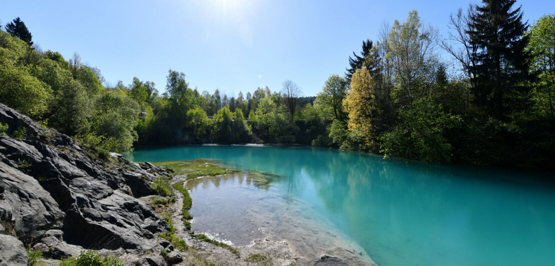 Ein kleiner, türkisblauer See, umrahmt von Bäumen