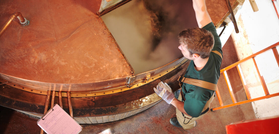 Der Blick von oben in einen geöffneten Sudkessel einer Brauerei, in dem Würze und Hopfen kochen