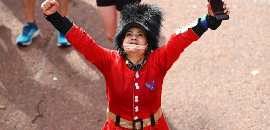 Eine Frau in roter Polizeitracht mit einer Teilnehmernummer des London Marathon reckt die Arme in die Höhe.