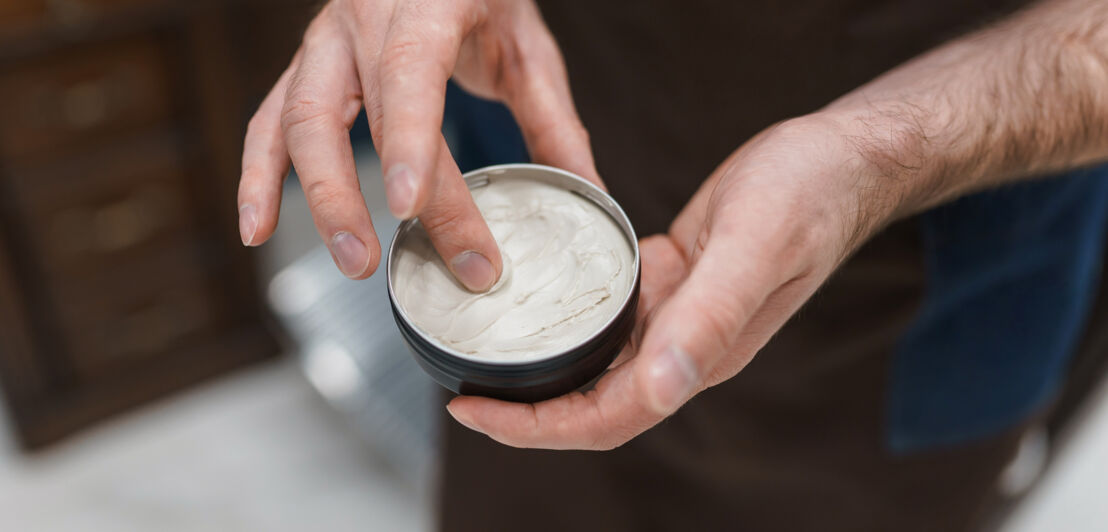 Mit dem Finger holt ein Mann Haarwachs aus einer geöffneten Dose