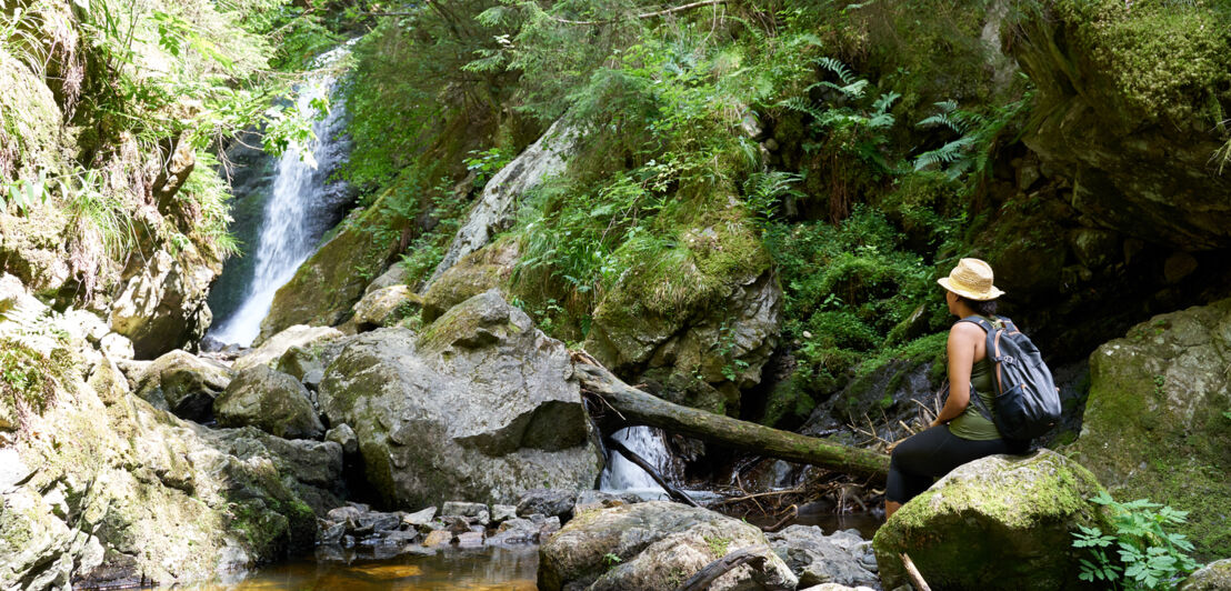 Eine Frau sitzt auf einem Felsen vor einem Wasserfall