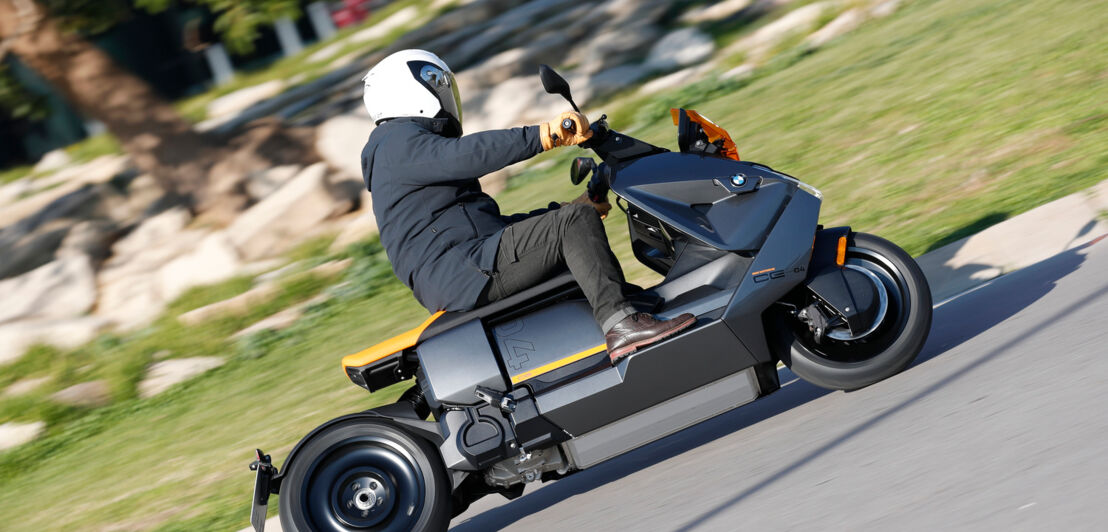 Ein grauer BMW CE 04 mit orangefarbenem Windschild fährt in einem Kreisverkehr.