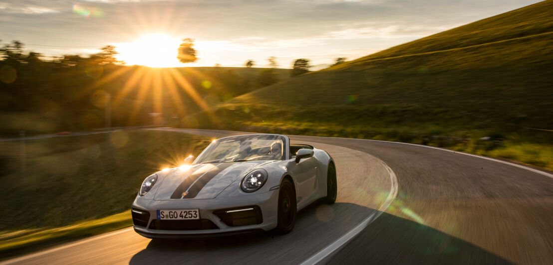 Ein graues Cabriolet fährt durch eine Kurve.