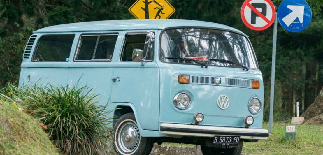 Ein hellblauer VW Bus T2 auf einer Straße mit bunten Straßenschildern