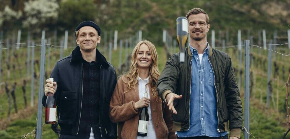 Matthias Schweighöfer, Juliane Eller und Joko Winterscheidt mit Weinflasche vor einem Weinberg