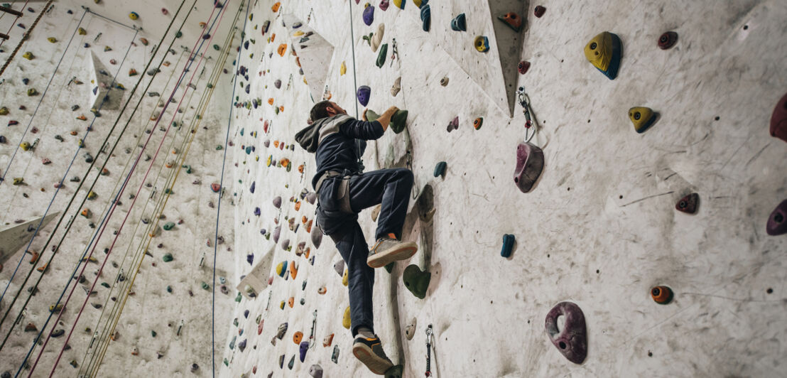 Unteransicht eines Mannes in voller Länge, der in einer Indoor-Halle klettert